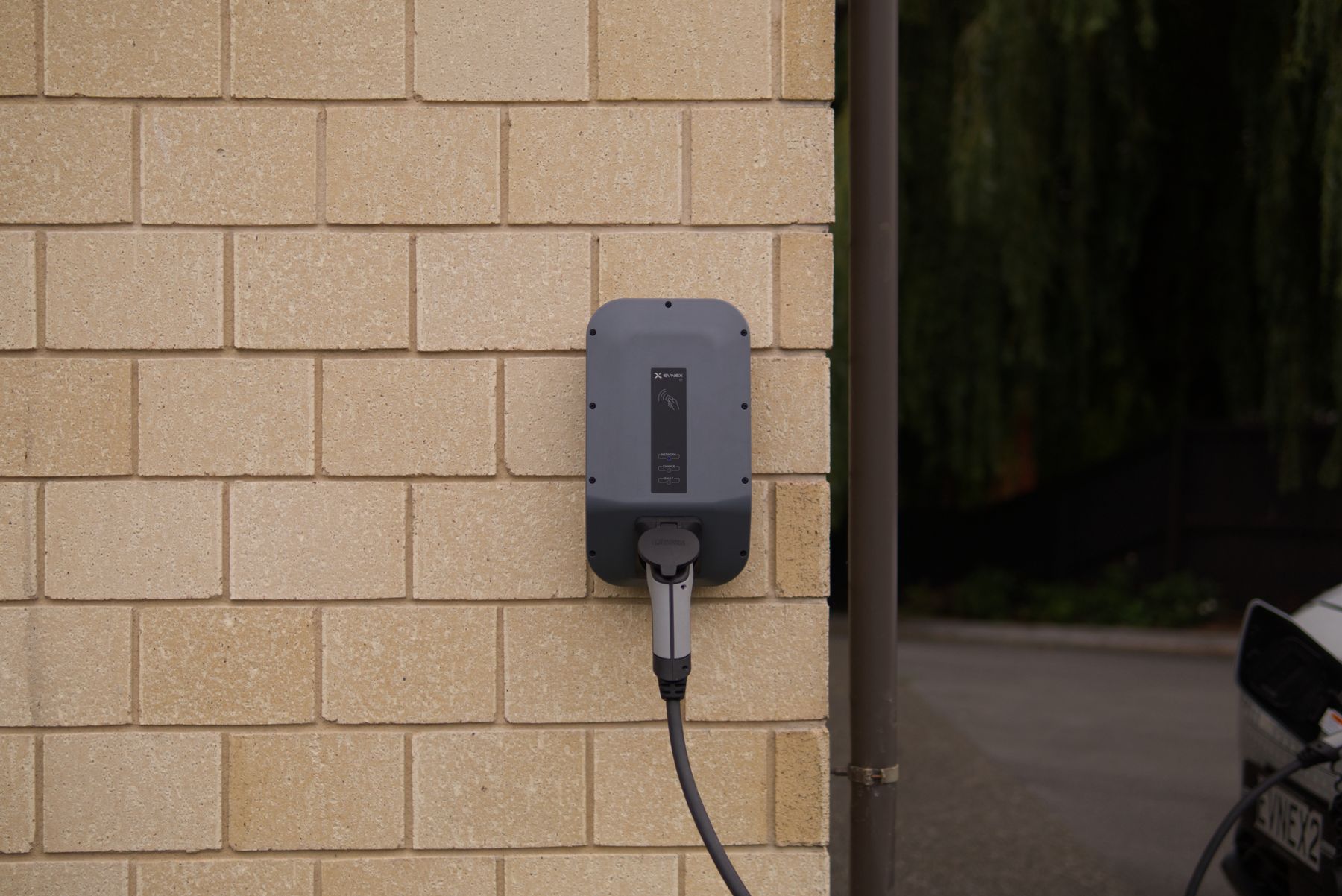 Electrician installing a Level 2 wall-mounted EV charger in a home garage beside an electric car at dusk